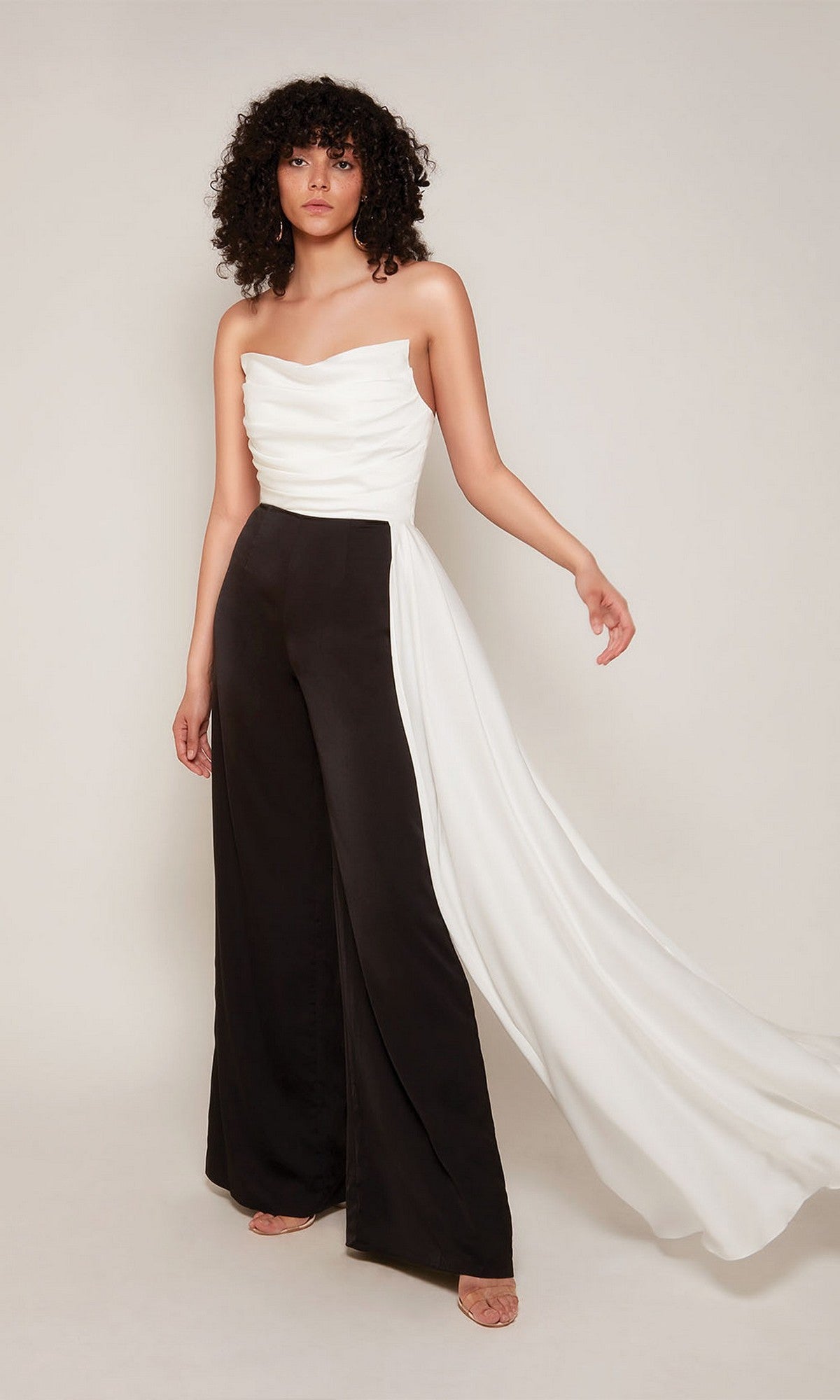 A woman stands against a plain background in the Alyce 70050 Long Formal Jumpsuit, featuring a strapless diamond white draped top with sash and wide-leg black pants.